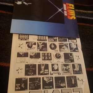 Puede incluir: Una portada del &aacute;lbum "Moody Blue" de Elvis Presley con un fondo azul y negro y un dise&ntilde;o de explosi&oacute;n de estrellas blancas. Debajo del &aacute;lbum hay un p&oacute;ster promocional con varias portadas de &aacute;lbumes de Elvis y el nombre "ELVIS" en letras grandes.