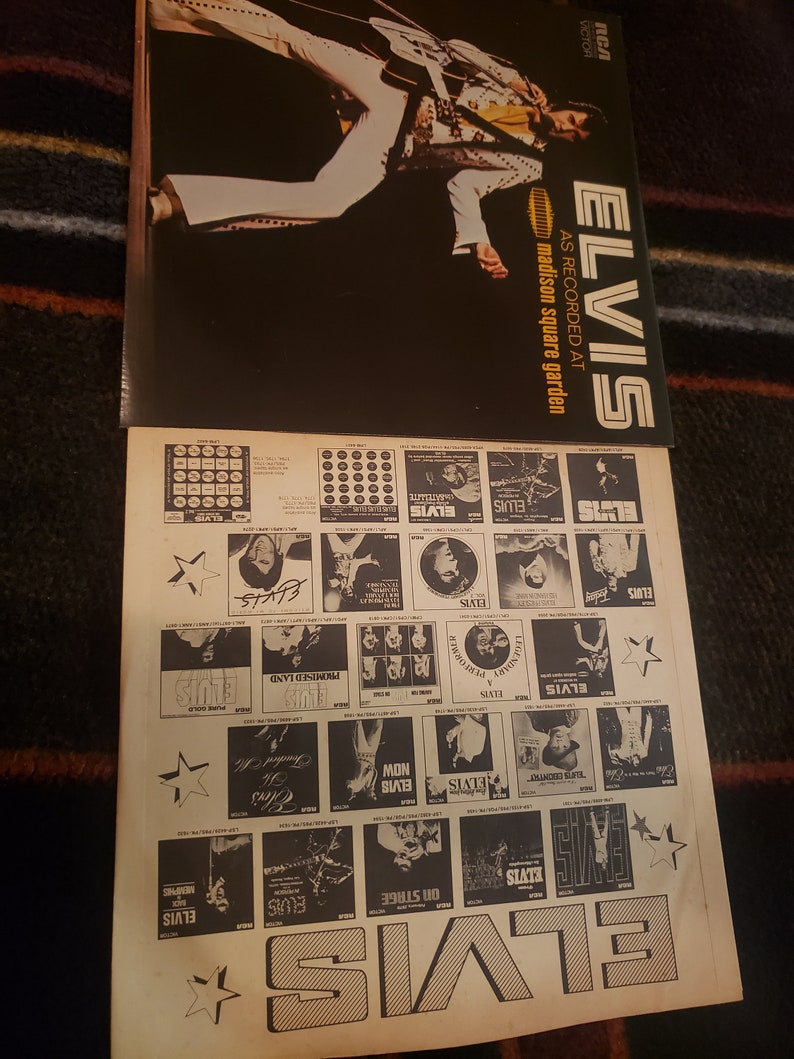 May include: A vintage vinyl record album cover featuring Elvis Presley. The cover is black with white text that reads "ELVIS" and "AS RECORDED AT MADISON SQUARE GARDEN". The album cover features a black and white photo of Elvis Presley performing on stage.
