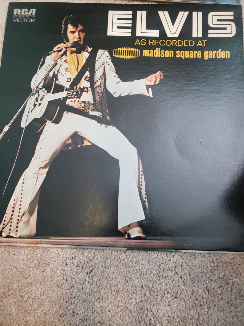 May include: A black vinyl record album cover featuring Elvis Presley in a white jumpsuit with a guitar. The album title is "Elvis As Recorded At Madison Square Garden".