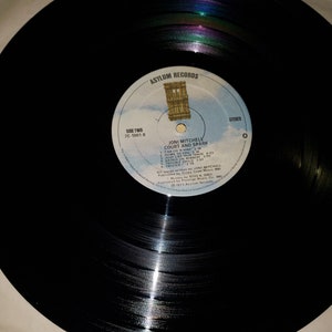 Puede incluir: Disco de vinilo negro con una etiqueta blanca. La etiqueta tiene el texto "Asylum Records", "Side Two", "7E-1001-B", "Joni Mitchell", "Court and Spark", "Car On A Hill", "Down To You", "Just Like This Train", "Raised On Robert", "Trouble Child", "Twisted", "All songs written by Joni Mitchell", "Published by Crazy Crow Music, BMI", "RO55 & GREY", "℗ 1973 Asylum Records", "Manufactured by Asylum Records, 4250  Camino  Real, Los Angeles, California 90065", "Stereo", y "0".
