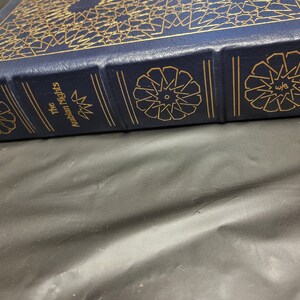 Puede incluir: Un libro de tapa dura azul con letras doradas y patrones decorativos. El t&iacute;tulo del libro es "Las mil y una noches".