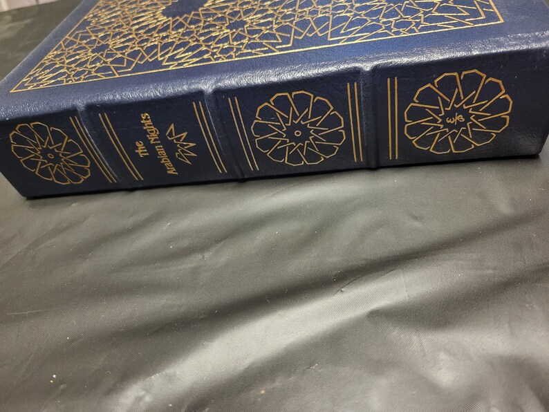 Puede incluir: Un libro de tapa dura azul con letras doradas y patrones decorativos. El t&iacute;tulo del libro es "Las mil y una noches".