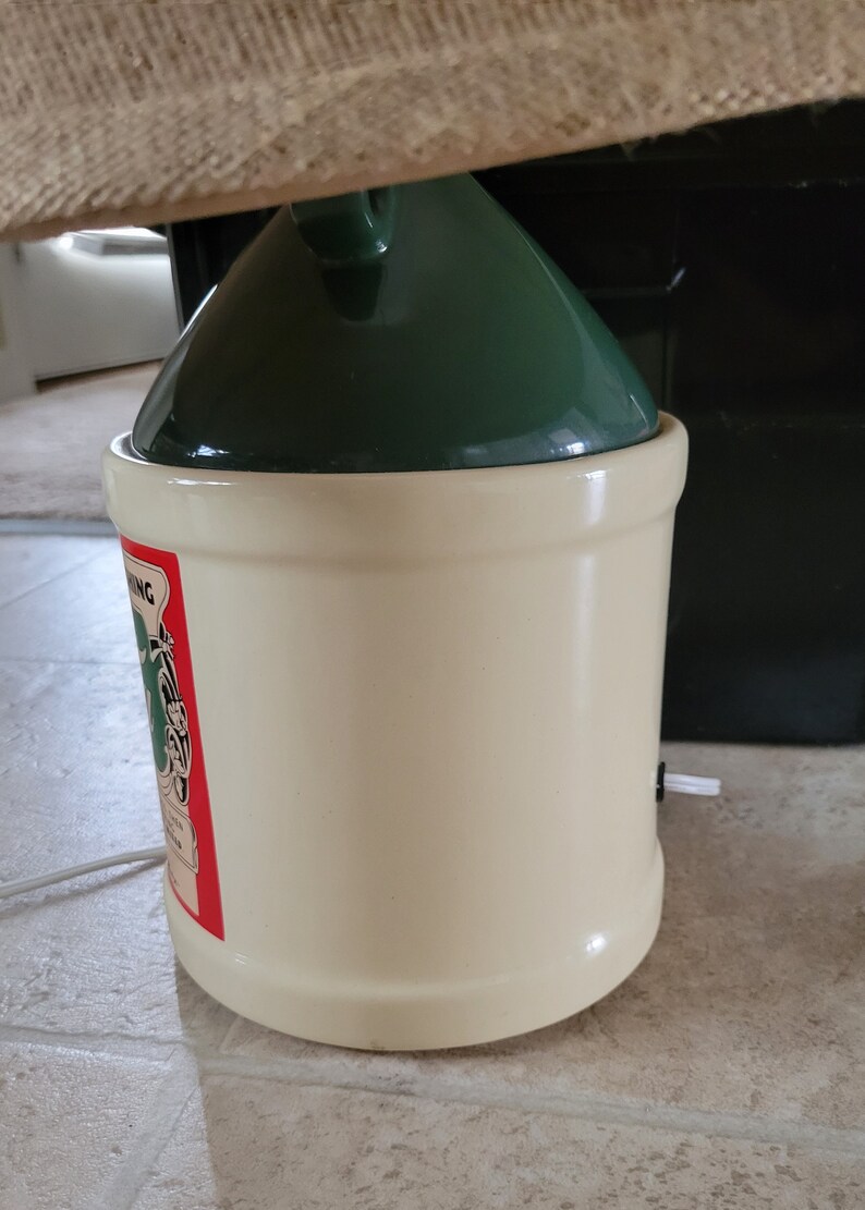 May include: A white ceramic crock with a green lid and a red and green label that says "Springing" with a picture of a frog. The crock has a white cord coming out of the bottom.