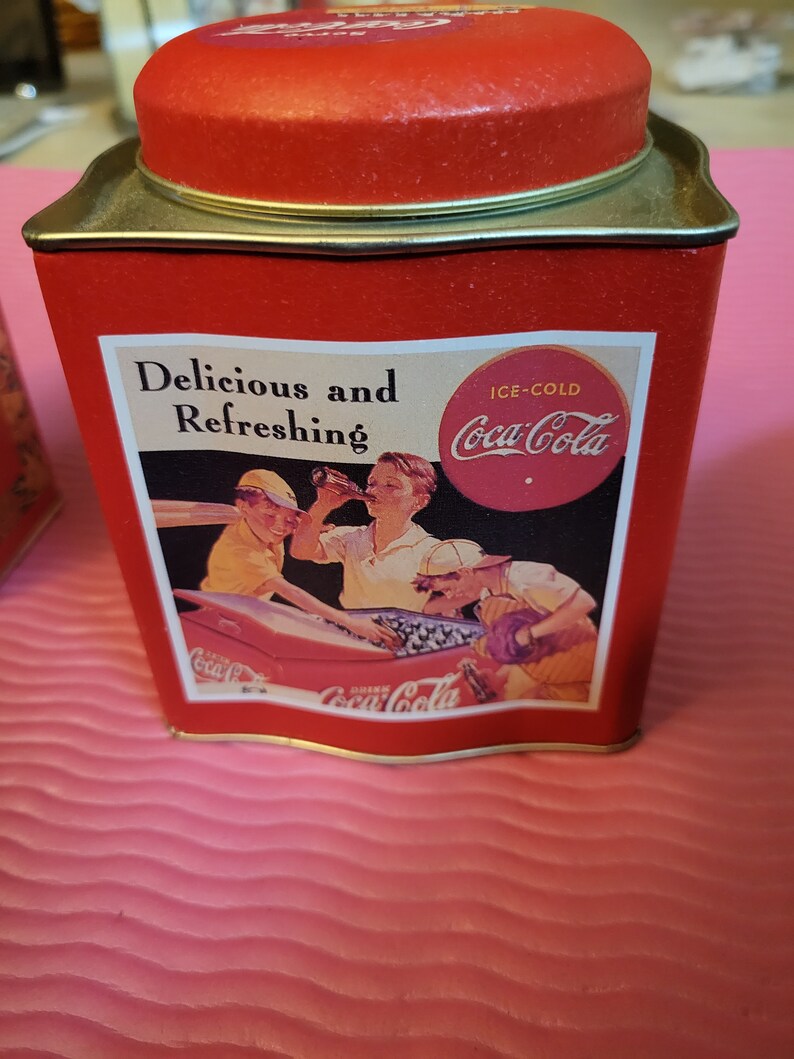 Puede incluir: Una lata roja de Coca-Cola con un dise&ntilde;o vintage que muestra a un grupo de personas disfrutando de Coca-Cola con hielo. La lata tiene el texto "Delicious and Refreshing" y "Ice-Cold Coca-Cola".