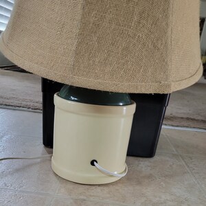 May include: A beige ceramic lamp base with a green top and a burlap lampshade. The lamp is plugged in and ready to use.