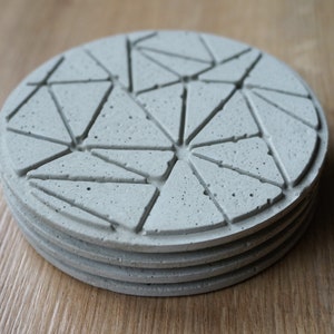 Könnte beinhalten: Set aus vier grauen Betonuntersetzern mit einem geometrischen Muster aus Dreiecken. Die Untersetzer sind übereinander gestapelt.