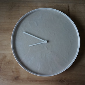 Könnte beinhalten: Eine runde Uhr mit weißem Rahmen, grauem Zifferblatt und weißen Zeigern. Die Uhr ist auf 10:10 eingestellt.