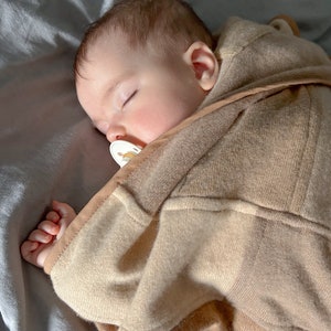 Könnte beinhalten: Ein Baby schläft tief und fest in einer braunen und weißen gestreiften Decke mit einem Schnuller im Mund.