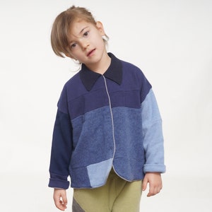 May include: A young person wearing a blue and light blue patchwork collared shirt with a green and brown patterned pants.