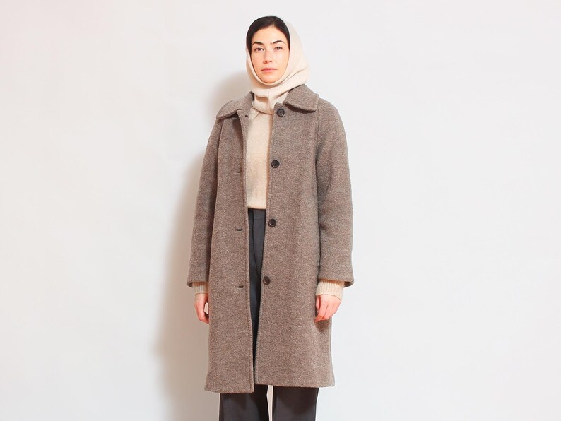 May include: A brown wool coat with a button closure and a white turtleneck sweater underneath. The person is wearing a white knitted hat.