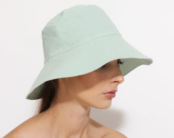 May include: A light green bucket hat made of a soft fabric. The hat has a wide brim and a simple design.