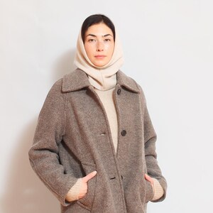 May include: A woman wearing a brown wool coat with a white turtleneck sweater and a white knit neck warmer.