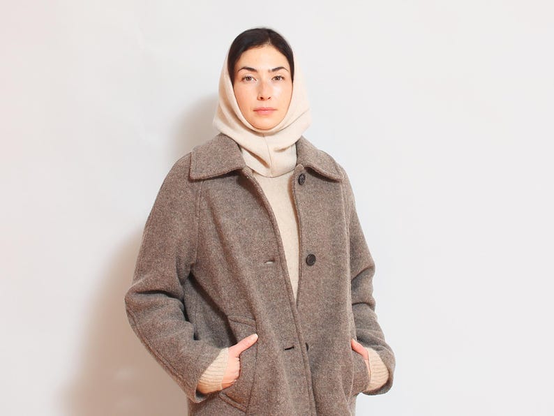 May include: A woman wearing a brown wool coat with a white turtleneck sweater and a white knit neck warmer.