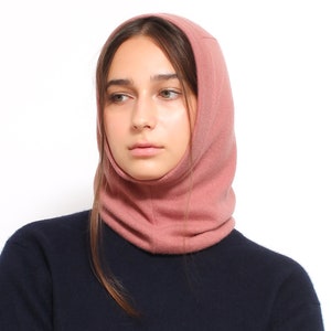 May include: A woman wearing a pink knitted neck warmer or snood. The neck warmer is made of a soft, warm material and is perfect for keeping warm in the winter.