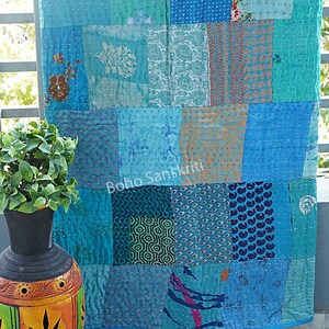 May include: A blue and turquoise kantha quilt with a patchwork design. The quilt is made from recycled saris and is hand-stitched. The quilt is hanging on a balcony railing. The text "boho sanskriti" is visible on the quilt.