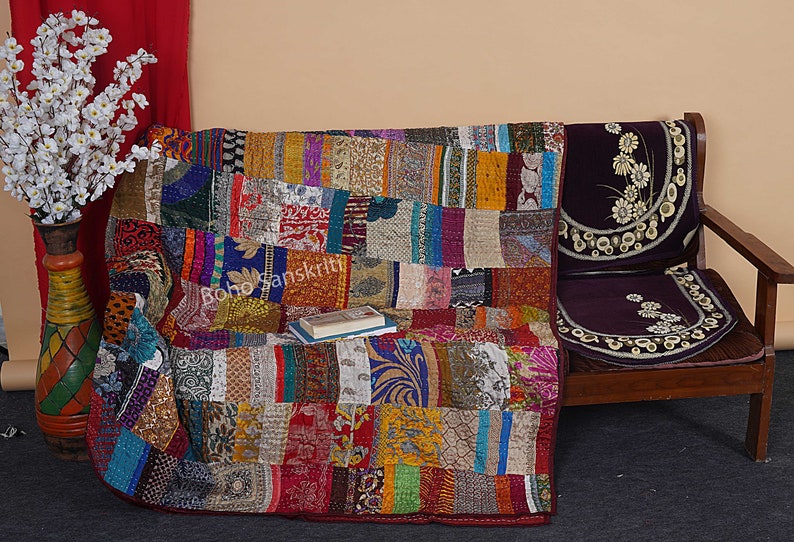 May include: A colorful patchwork quilt made from recycled saris, featuring a variety of patterns and colors. The quilt is draped over a wooden chair with a purple cushion. The quilt is approximately 60 inches by 80 inches.