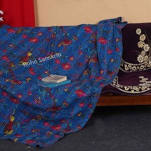 May include: A blue kantha quilt with a floral pattern and white stitching. The quilt is draped over a wooden bench with a purple cushion. The text "boho sanskriti" is visible on the quilt.