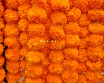 Op de afbeelding: Een close-up van talrijke feloranje goudsbloemen, dicht op elkaar gepakt. De afbeelding benadrukt de textuur en kleur van de bloemen, waarbij elke bloem meerdere lagen bloemblaadjes laat zien. De tekst "BohoSanskriti" is zichtbaar.