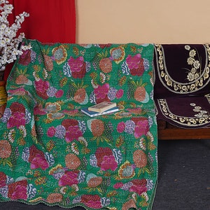 May include: A green kantha quilt with a floral and pineapple pattern. The quilt is draped over a wooden bench with a purple cushion cover.