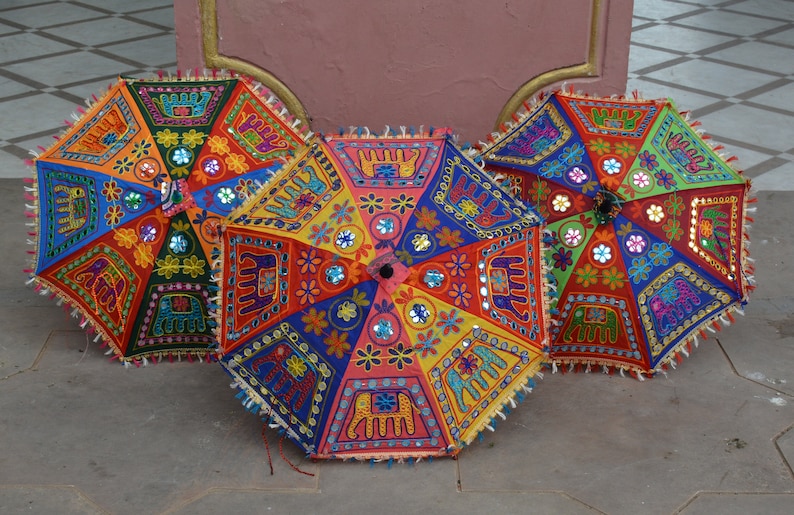 Puede incluir: Tres paraguas coloridos con bordados intrincados y adornos de espejo. Los paraguas est&aacute;n hechos de tela y tienen un dise&ntilde;o tradicional indio.