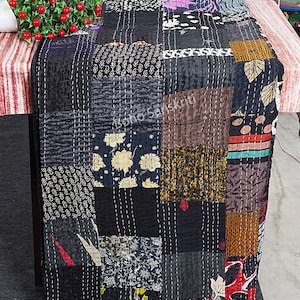 Może przedstawiać: Czarno-biała kołdra patchworkowa z różnymi wzorami kwiatowymi i geometrycznymi. Kołdra jest wykonana z recyklingowanych sari i szyta ręcznie. "Boho Sanskriti" jest nadrukowane na kołdrze.