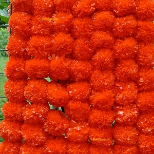 May include: A garland of bright orange marigold flowers, made of paper, with the text "BohoSanskruti" printed on it.