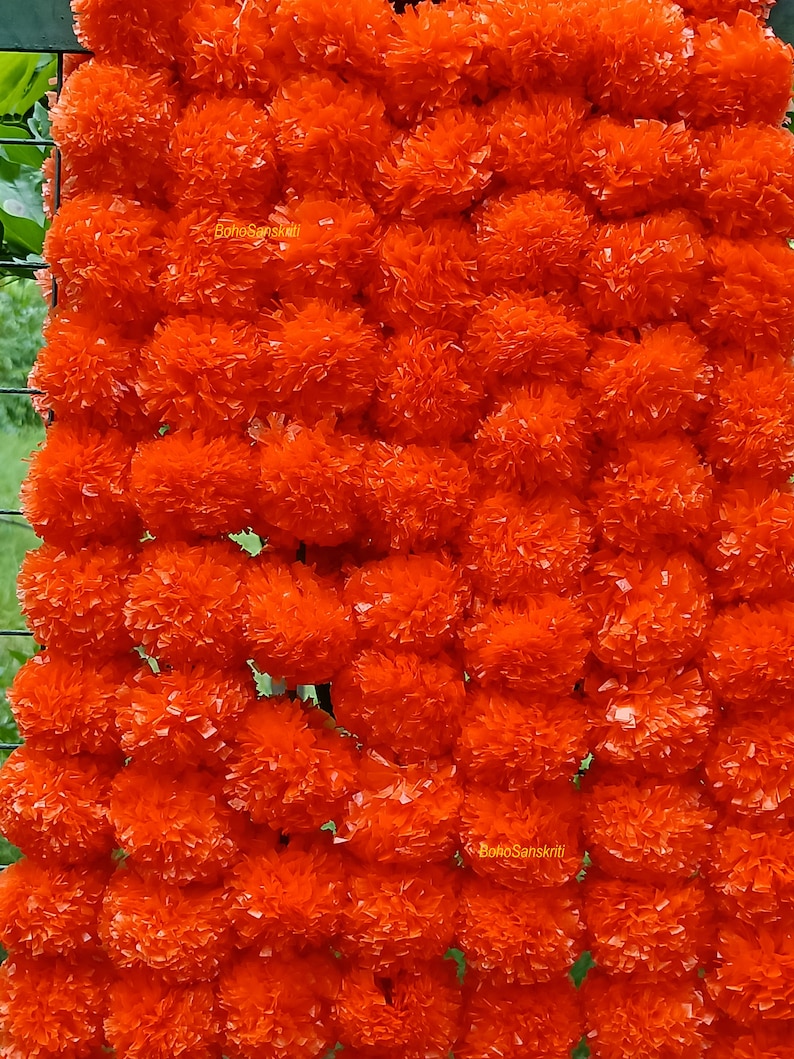 May include: A garland of bright orange marigold flowers, made of paper, with the text "BohoSanskruti" printed on it.