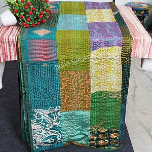 May include: A patchwork quilt featuring a mix of colours and patterns, including green, blue, yellow, and purple. The quilt is crafted from recycled saris and is hand-stitched.
