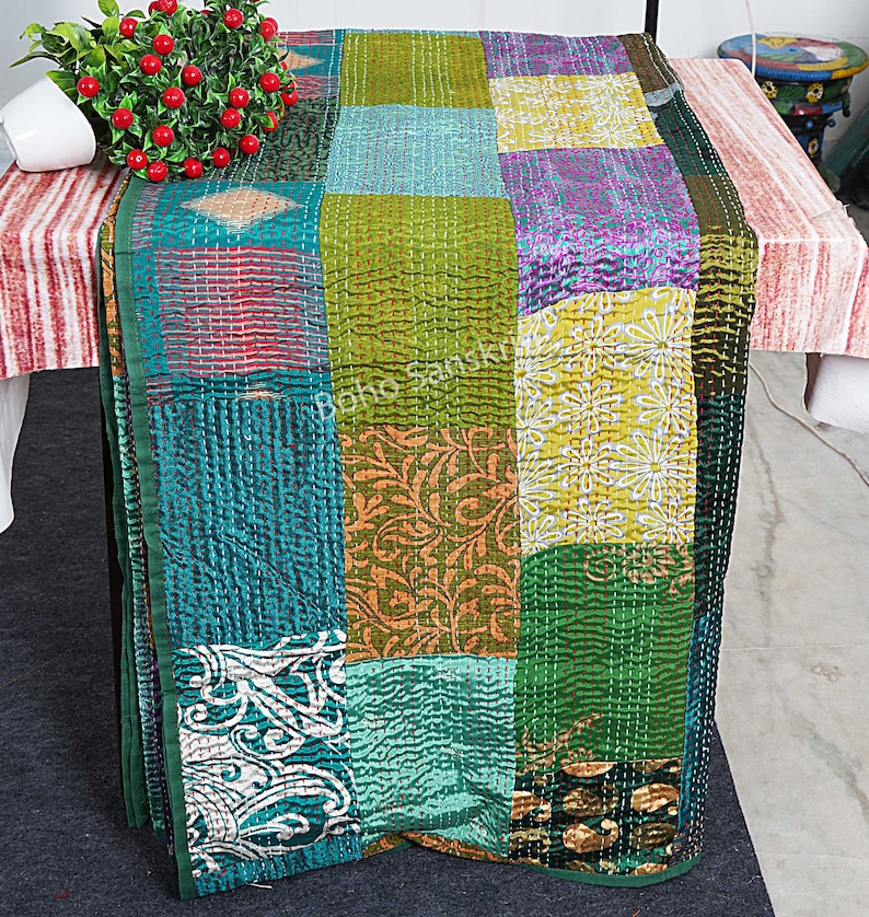 May include: A patchwork quilt featuring a mix of colours and patterns, including green, blue, yellow, and purple. The quilt is crafted from recycled saris and is hand-stitched.