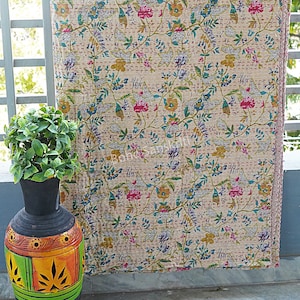 May include: A cream-colored kantha quilt with a floral pattern in shades of pink, blue, green, and yellow. The quilt has a pink border and is made of cotton.
