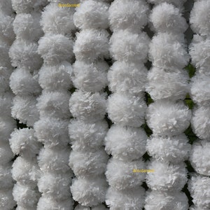 May include: White paper flower garlands, also known as "Gajra", are strung together in rows. The garlands are made of white paper and are arranged in a symmetrical pattern. The garlands are used for decoration and are often seen at weddings and other special occasions.
