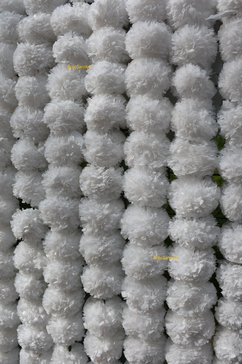 May include: White paper flower garlands, also known as "Gajra", are strung together in rows. The garlands are made of white paper and are arranged in a symmetrical pattern. The garlands are used for decoration and are often seen at weddings and other special occasions.