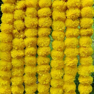 May include: A garland of bright yellow marigold flowers, strung together in a long row. The flowers are arranged in a symmetrical pattern, creating a visually appealing and festive decoration.