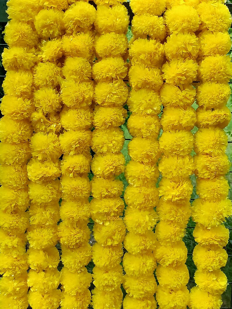 May include: A garland of bright yellow marigold flowers, strung together in a long row. The flowers are arranged in a symmetrical pattern, creating a visually appealing and festive decoration.