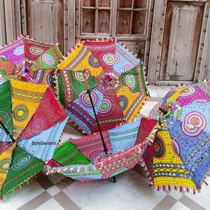 May include: Five colorful umbrellas with intricate patterns and embroidery. The umbrellas are made of fabric and have a wooden handle. The umbrellas are arranged in a circle on a tiled floor.