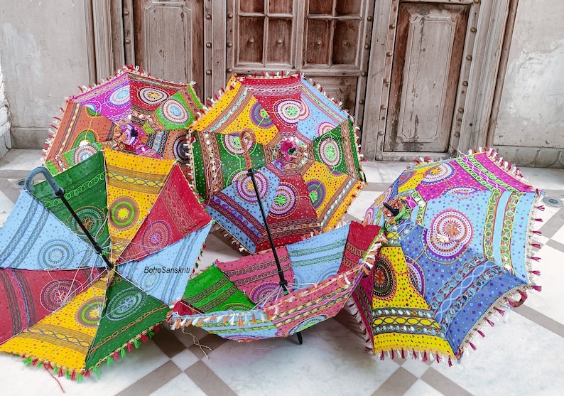 May include: Five colorful umbrellas with intricate patterns and embroidery. The umbrellas are made of fabric and have a wooden handle. The umbrellas are arranged in a circle on a tiled floor.