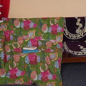 May include: A green kantha quilt with a floral and pineapple print. The quilt is draped over a wooden chair with a purple cushion.
