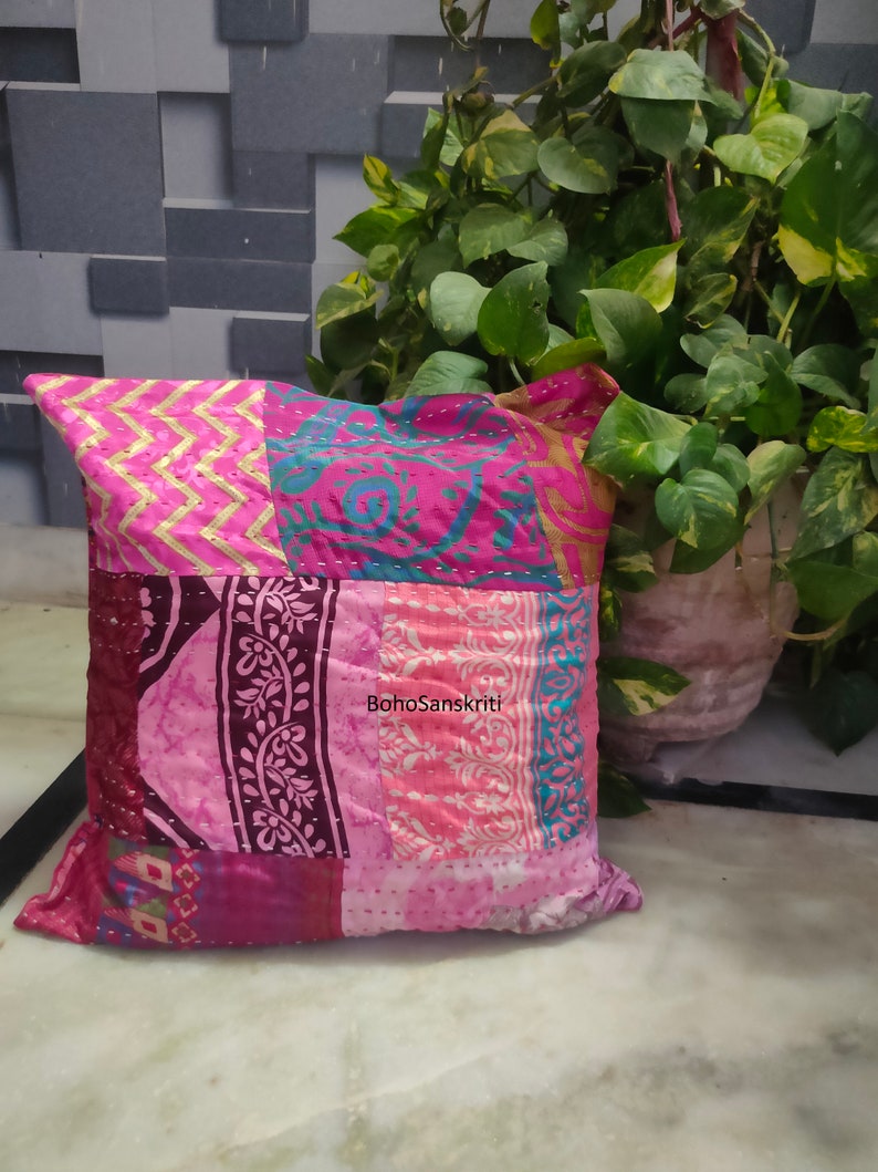 May include: A patchwork pillow with a variety of pink and magenta fabrics. The pillow features a mix of patterns, including zigzags, floral designs, and stripes. The text "BohoSanskriti" is visible on the pillow.