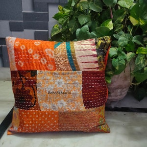 May include: Square patchwork pillow with orange, brown, and floral patterns. The pillow features visible stitching and a mix of fabrics. The text "BohoSanskriti" is printed on the pillow.