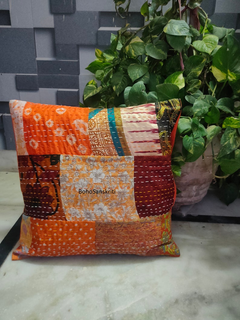 May include: Square patchwork pillow with orange, brown, and floral patterns. The pillow features visible stitching and a mix of fabrics. The text "BohoSanskriti" is printed on the pillow.