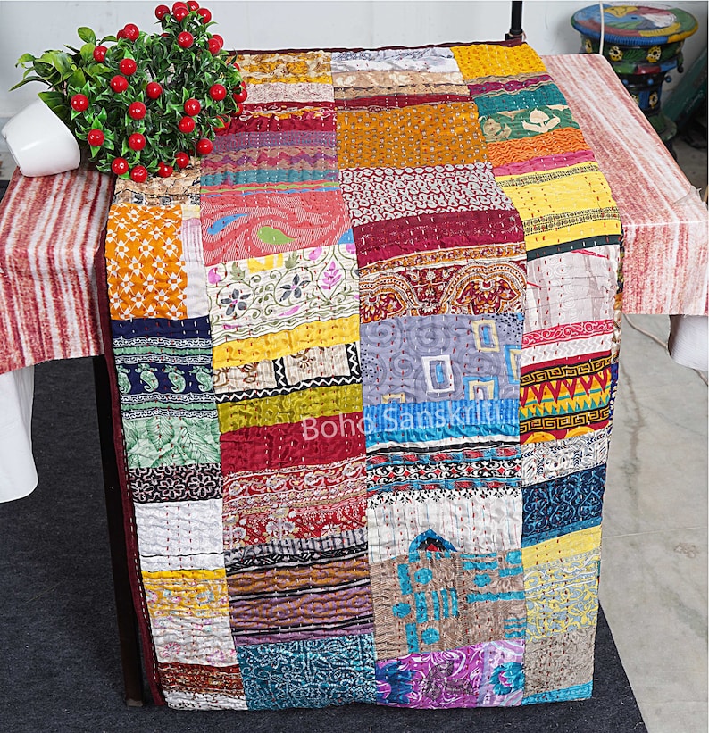 May include: A colourful patchwork quilt made from recycled saris. The quilt is made up of squares of different fabrics, each with a unique pattern and colour. The quilt is a beautiful example of Indian craftsmanship.
