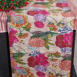 May include: A beige table runner with a floral pattern in shades of pink, green, orange, and blue. The runner is quilted and has a subtle sheen.