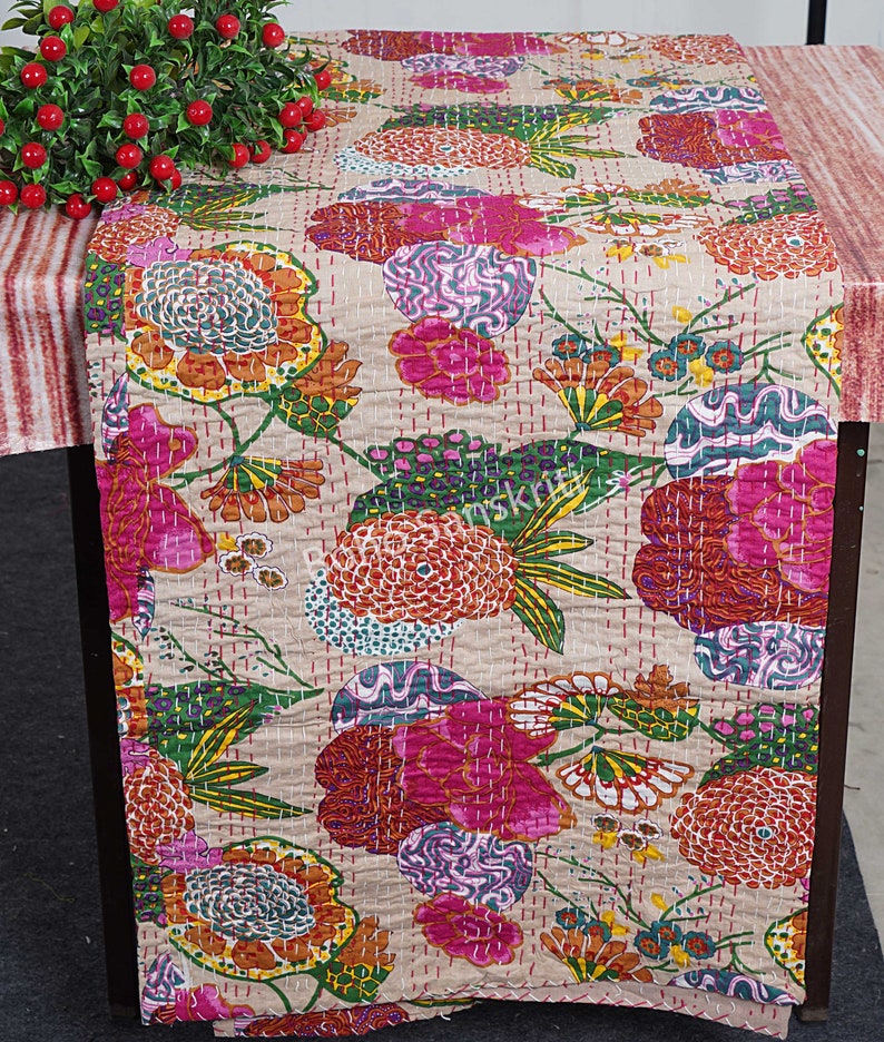May include: A beige table runner with a floral pattern in shades of pink, green, orange, and blue. The runner is quilted and has a subtle sheen.
