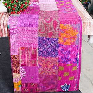 May include: A pink patchwork table runner made from silk fabric with various patterns. The runner is approximately 46 cm wide and 183 cm long.