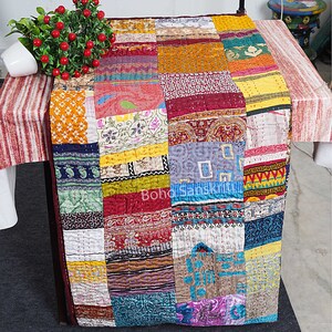 May include: A colorful patchwork quilt made from recycled saris. The quilt is made up of squares of different fabrics, each with a unique pattern and color. The quilt is a beautiful example of Indian craftsmanship.