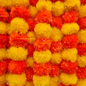 May include: A garland of yellow and orange paper marigolds, also known as marigold pom poms, arranged in a repeating pattern. The garland is a traditional Indian decoration used for festivals and celebrations.