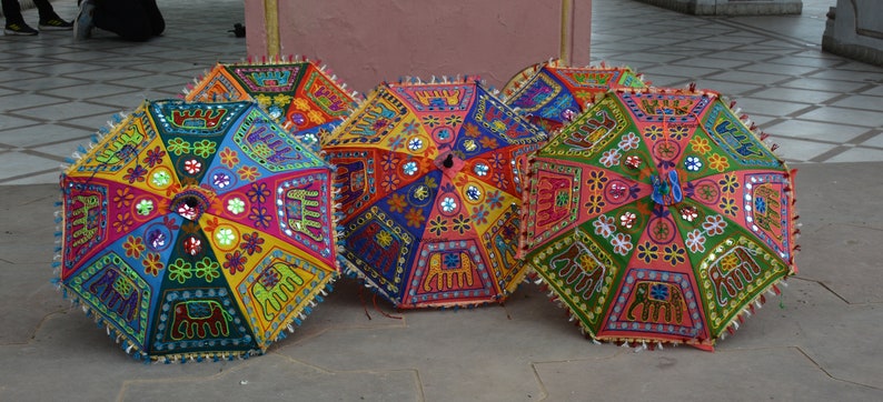 Puede incluir: Cuatro paraguas coloridos con bordados intrincados y adornos de espejo. Los paraguas est&aacute;n decorados con elefantes, flores y patrones geom&eacute;tricos. Los paraguas est&aacute;n hechos de tela y tienen un mango de madera.
