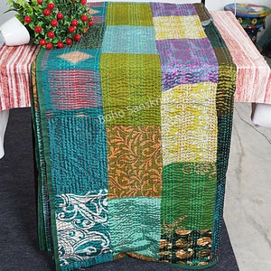 Könnte beinhalten: Ein Patchwork-Tischläufer mit verschiedenen grünen, türkisfarbenen und gelben Quadraten. Der Läufer weist aufwendige Nähte und eine Mischung aus floralen und geometrischen Mustern auf. Die Kanten sind mit einem dunkelgrünen Rand versehen.