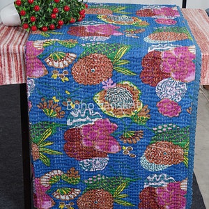 May include: A blue table runner with a floral pattern in shades of pink, orange, green, and brown. The runner is made of cotton and has a quilted texture.