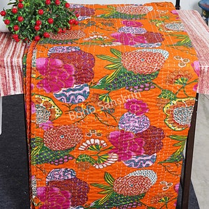 K&ouml;nnte beinhalten: Orangefarbene Kantha-Steppdecke mit einem floralen Muster in Rosa-, Gr&uuml;n- und Lilat&ouml;nen. Die Decke ist aus Baumwolle und hat ein handgesticktes Design.